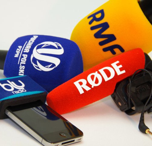 Colorful foam microphone covers with logos from RØDE, RMF, blu radio, and other broadcasters in a studio setup.