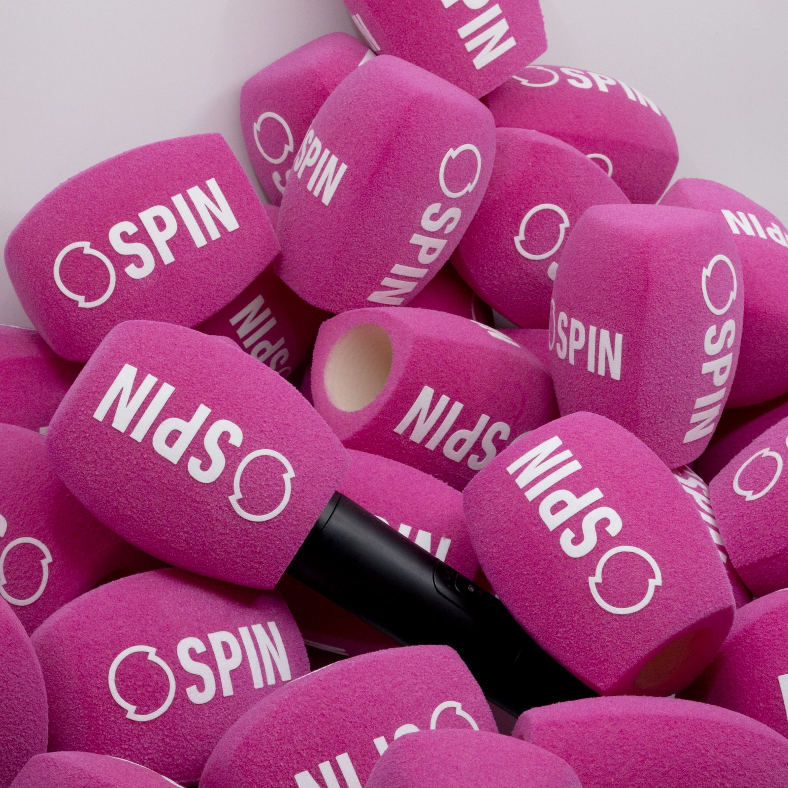 Pile of bright pink foam microphone covers branded with the SPIN radio logo.