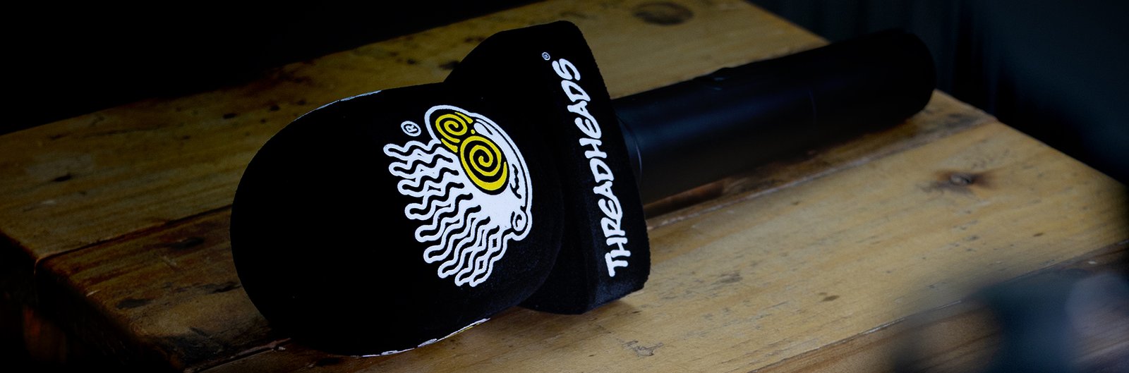 Custom black microphone windscreen with "Threadheads" branding and a yellow and white octopus logo, on a handheld microphone resting on a rustic wooden table.