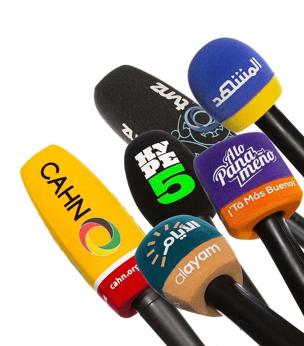 Collection of various custom branded microphone windscreens on microphones, featuring different shapes, colours, and international logos (CAHN, Hype 5, Alayam) against a white background.